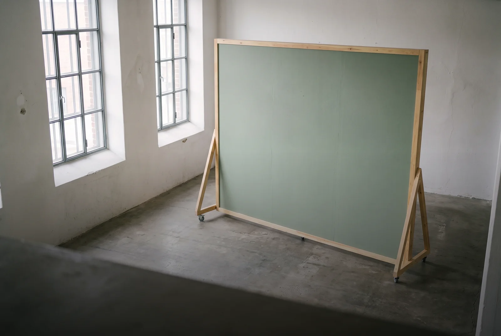 An empty whitewashed room with tall mill windows and a large green board on a wooden easel