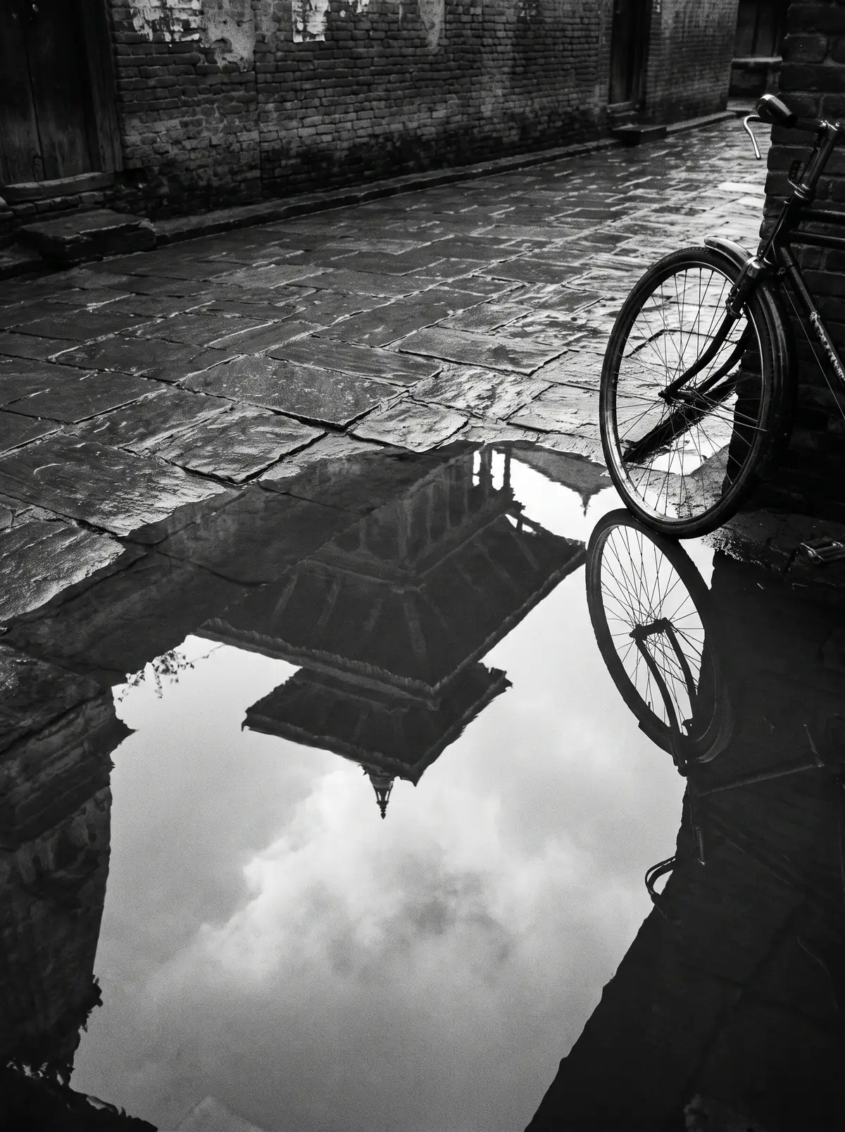 A temple roof reflected in a rain puddle beside a parked bicycle